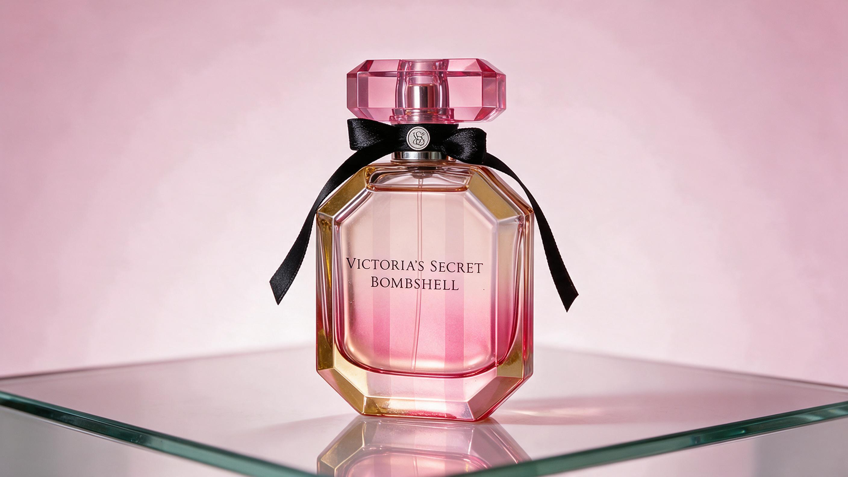 an elegant pink and gold gradient perfume bottle with a bow-shaped cap standing on a reflective glass vanity surface, so