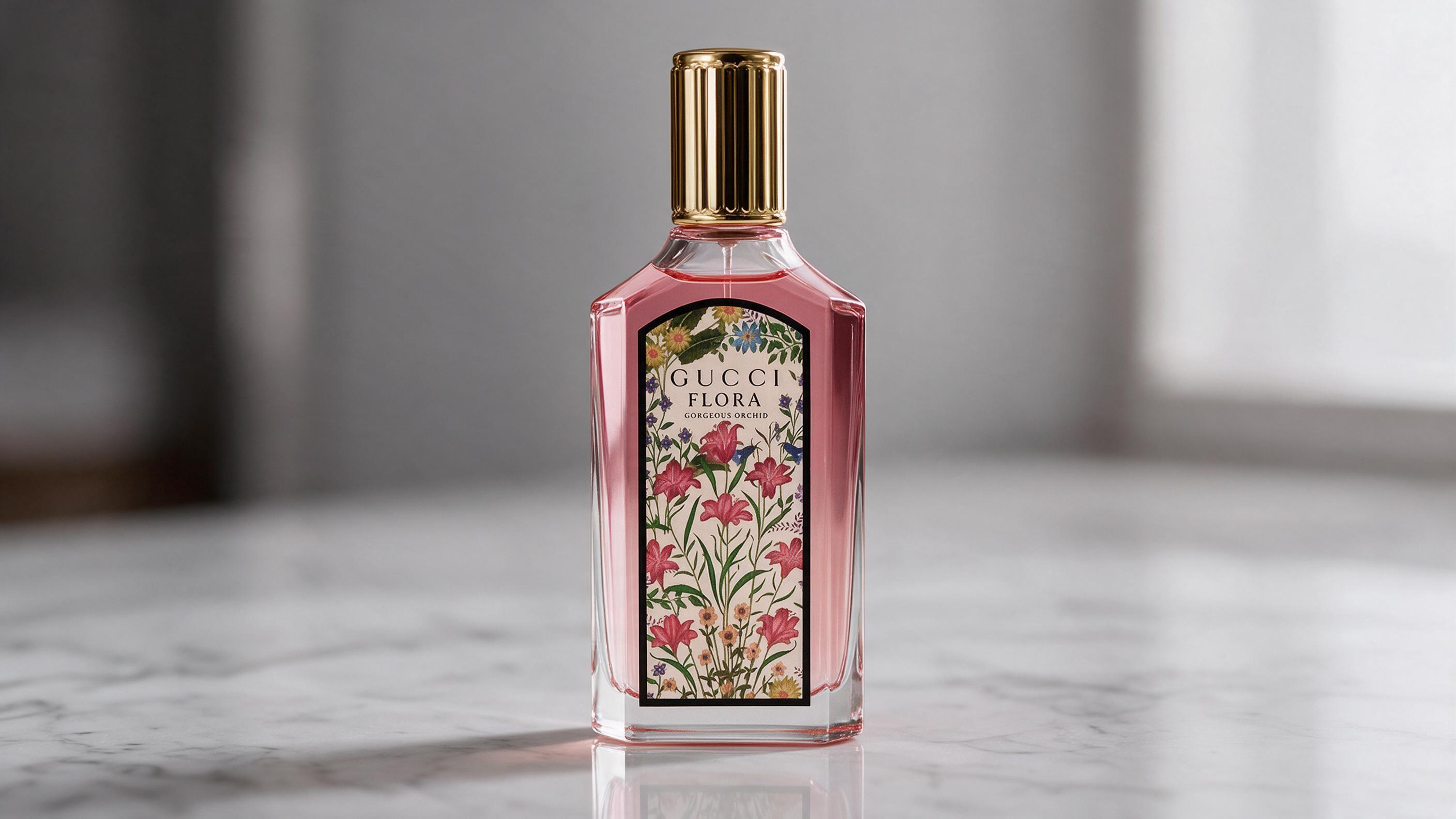 Tall elegant glass perfume bottle labeled Gucci Flora Gorgeous Orchid with a soft pink gradient liquid, decorative facet